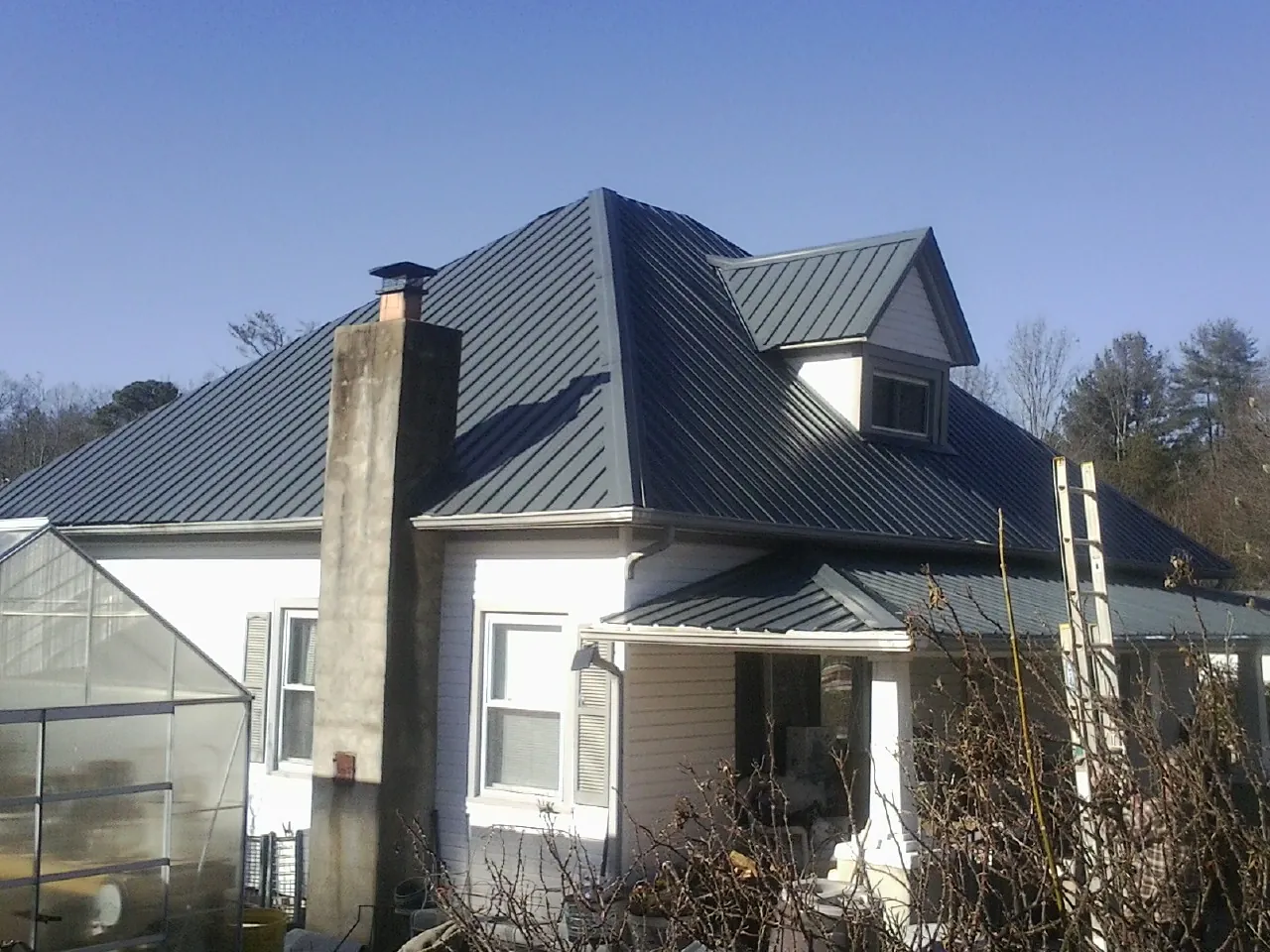 Dark blue standing seam metal roof on a white farmhouse with dormer — Slate & Tile Roof Repair by Roofing Brothers in Lumber Bridge