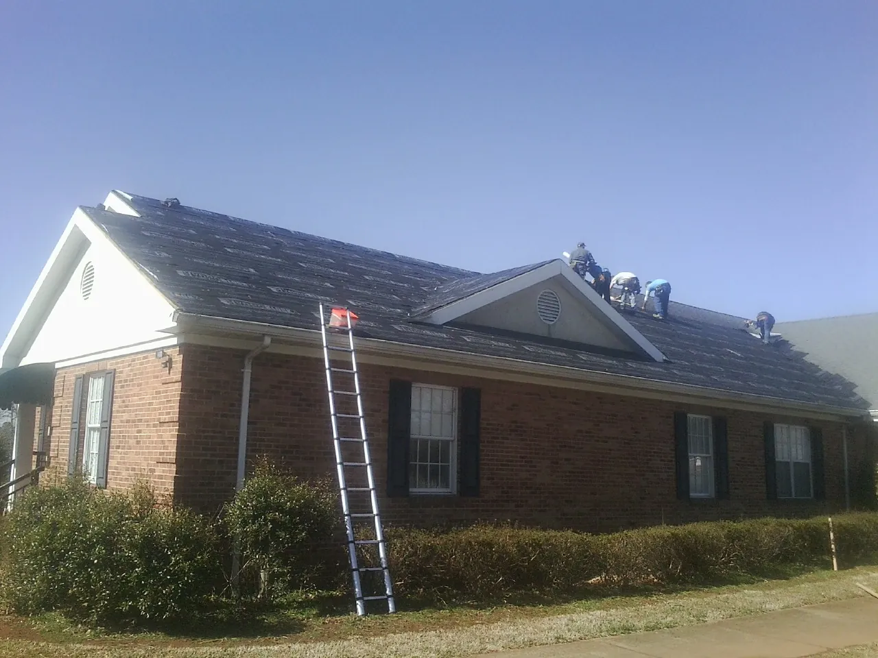 Crew tearing shingles off a brick ranch roof with a ladder set — Metal Roof Repair work by our crew in Lumber Bridge