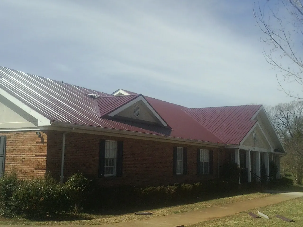 Red metal roof with gabled entries on a long brick building, from a Hail Damage Roof Repair job in Lumber Bridge