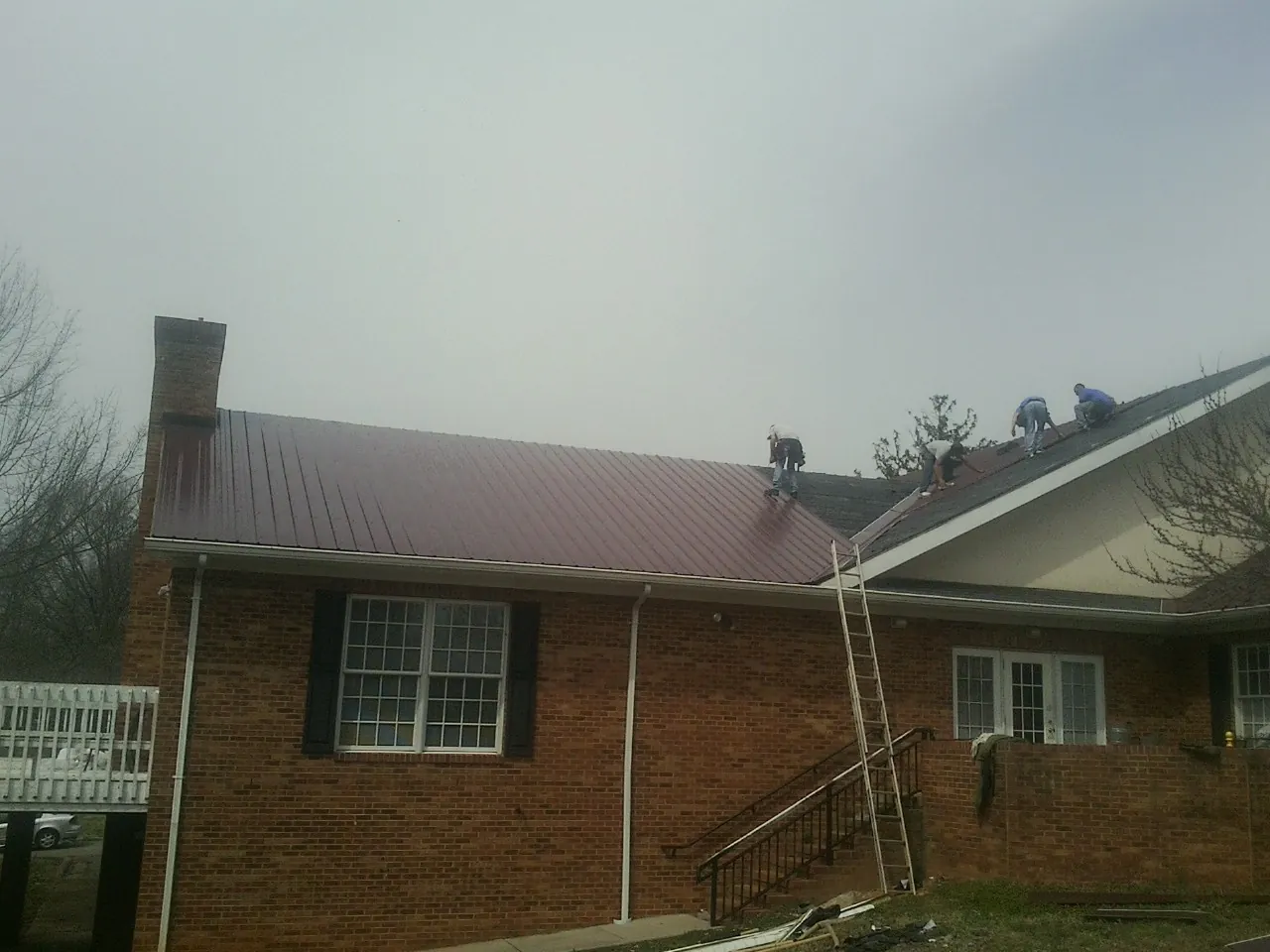 Crew setting red metal roofing panels on a brick home in Lumber Bridge