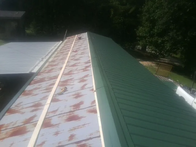 Old rusted panels beside newly installed green metal roofing — Wind Damage Roof Repair by Roofing Brothers in Lumber Bridge