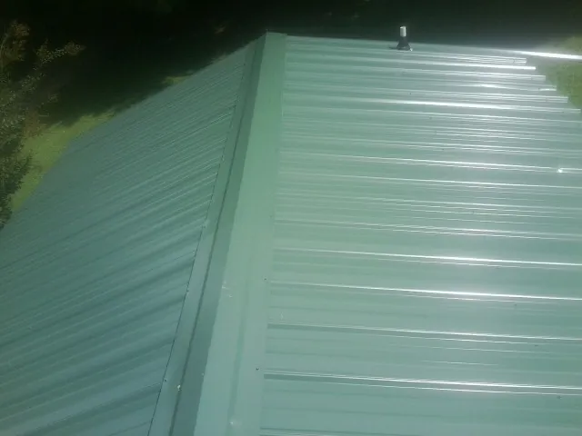 New green metal panels meeting at the ridge of a roof — Flat Roof Repair work by our crew in Lumber Bridge