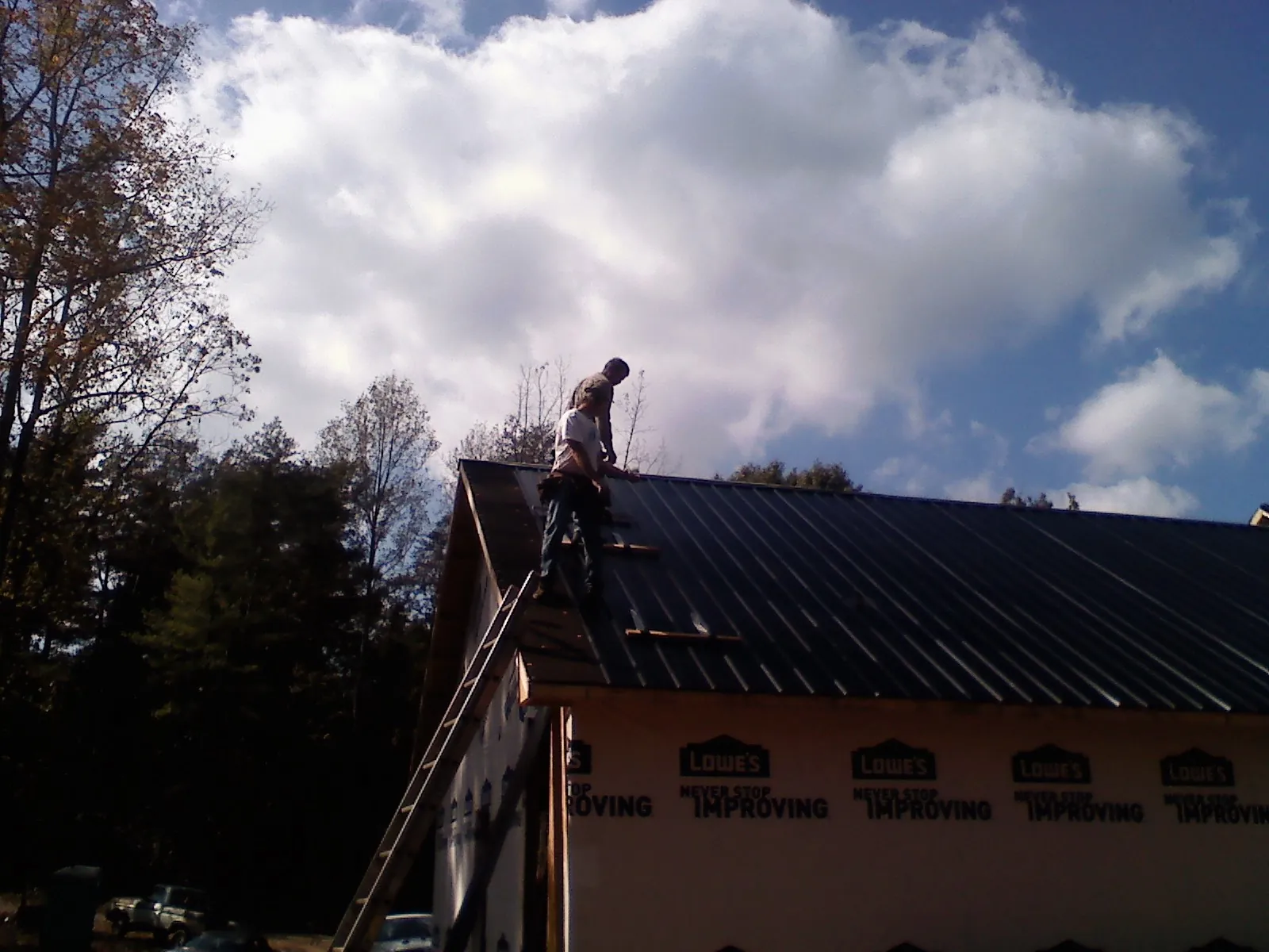 Roofer fastening dark metal panels high against a cloudy sky, from a Roof Inspection job in Lumber Bridge