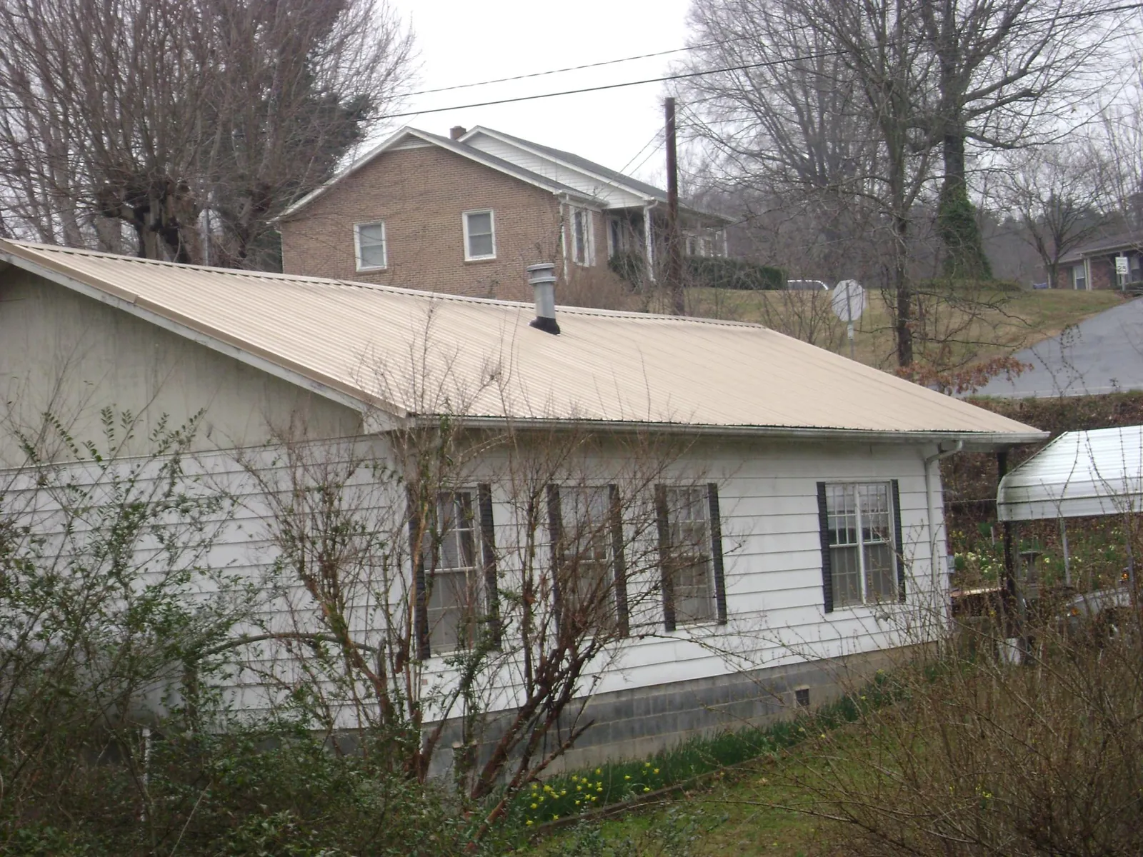 Tan metal roof on a white sided house set into a hillside — Commercial Roofing by Roofing Brothers in Lumber Bridge